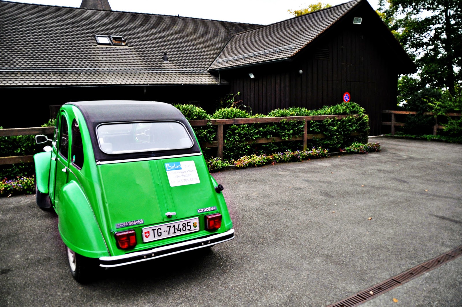 A bright green Citroen 2CV parked outside a wooden Swiss house