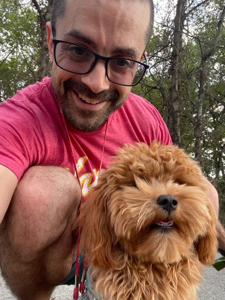 Adam and Poppy the Cavapoo smiling together outside — the man who grabbed a snake by the tail and the dog who ran up and down the yard smiling for three hours straight.