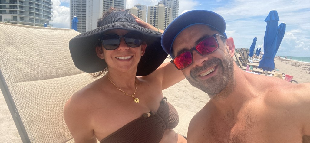 Nicole and Adam smiling on Miami Beach the day their house went under contract — two people who chose one life and are living every single bit of it.
