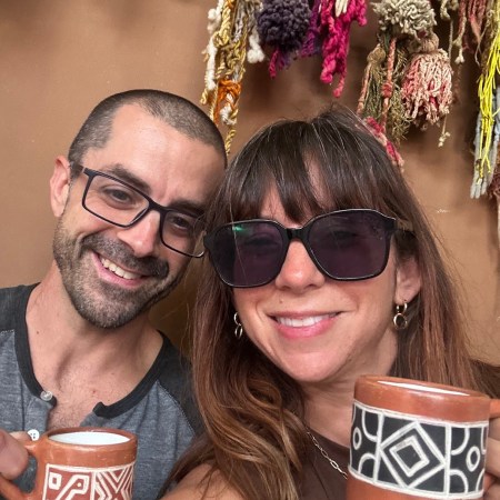 Nicole and Adam smiling together holding matching handmade ceramic mugs — two people who wake up every morning excited about what is coming next.