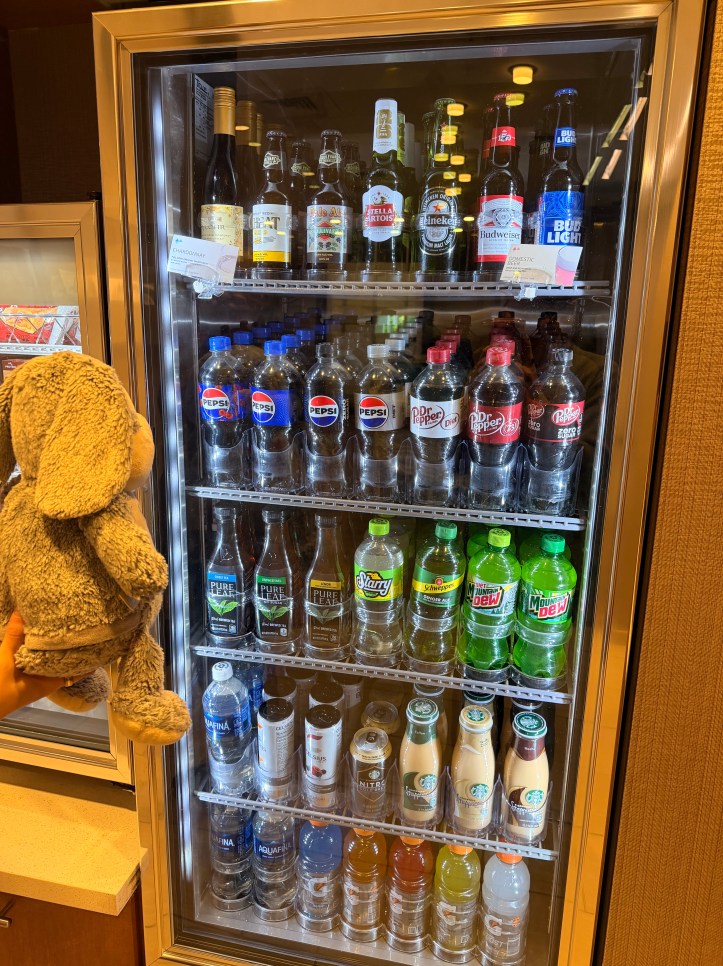 Bun Bun the stuffed bunny browsing the drink selection at the Springhill Suites Lenexa hotel market during her extended solo stay.