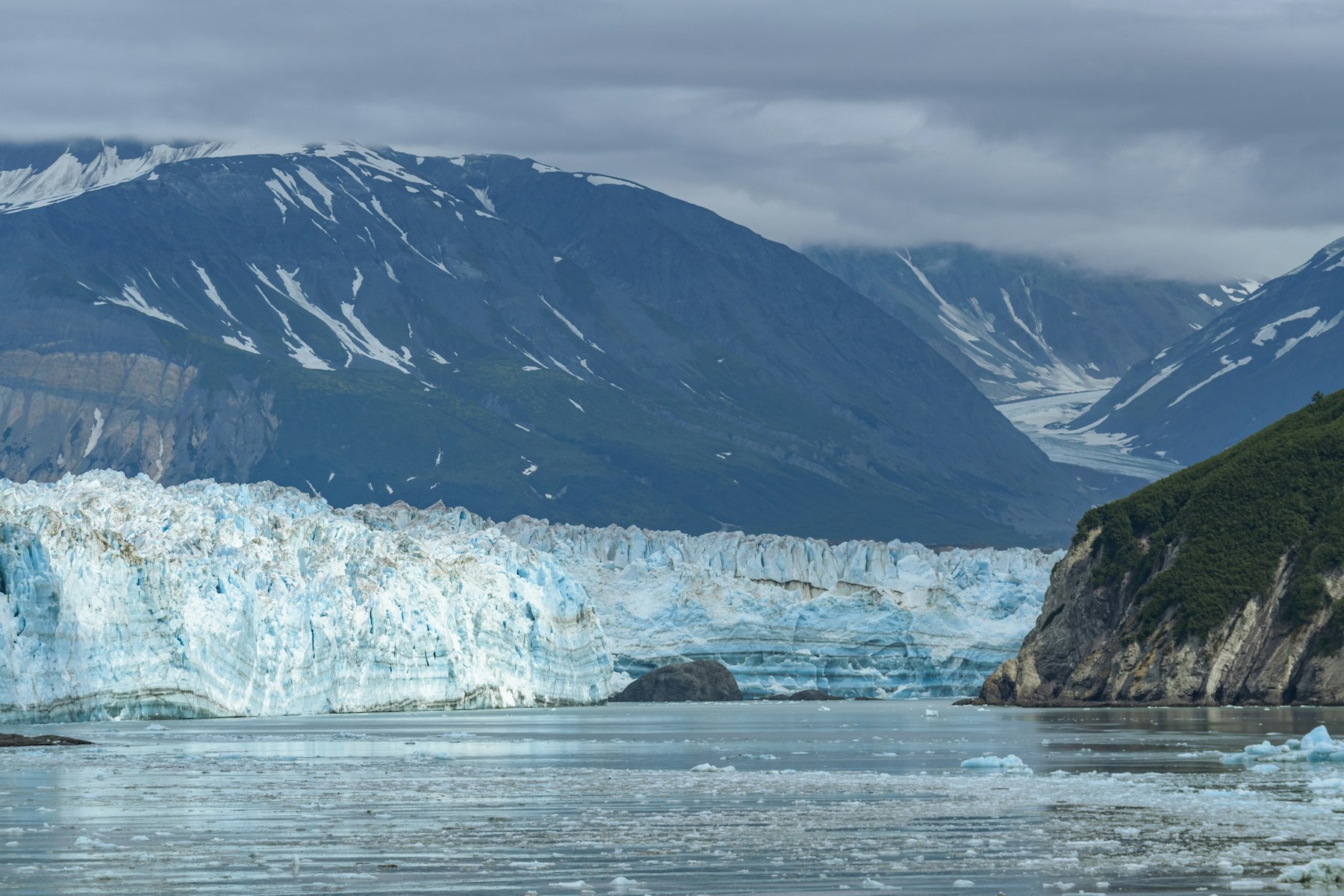 The blue calving face of a tidewater glacier meeting the sea below a dark mountain ridge