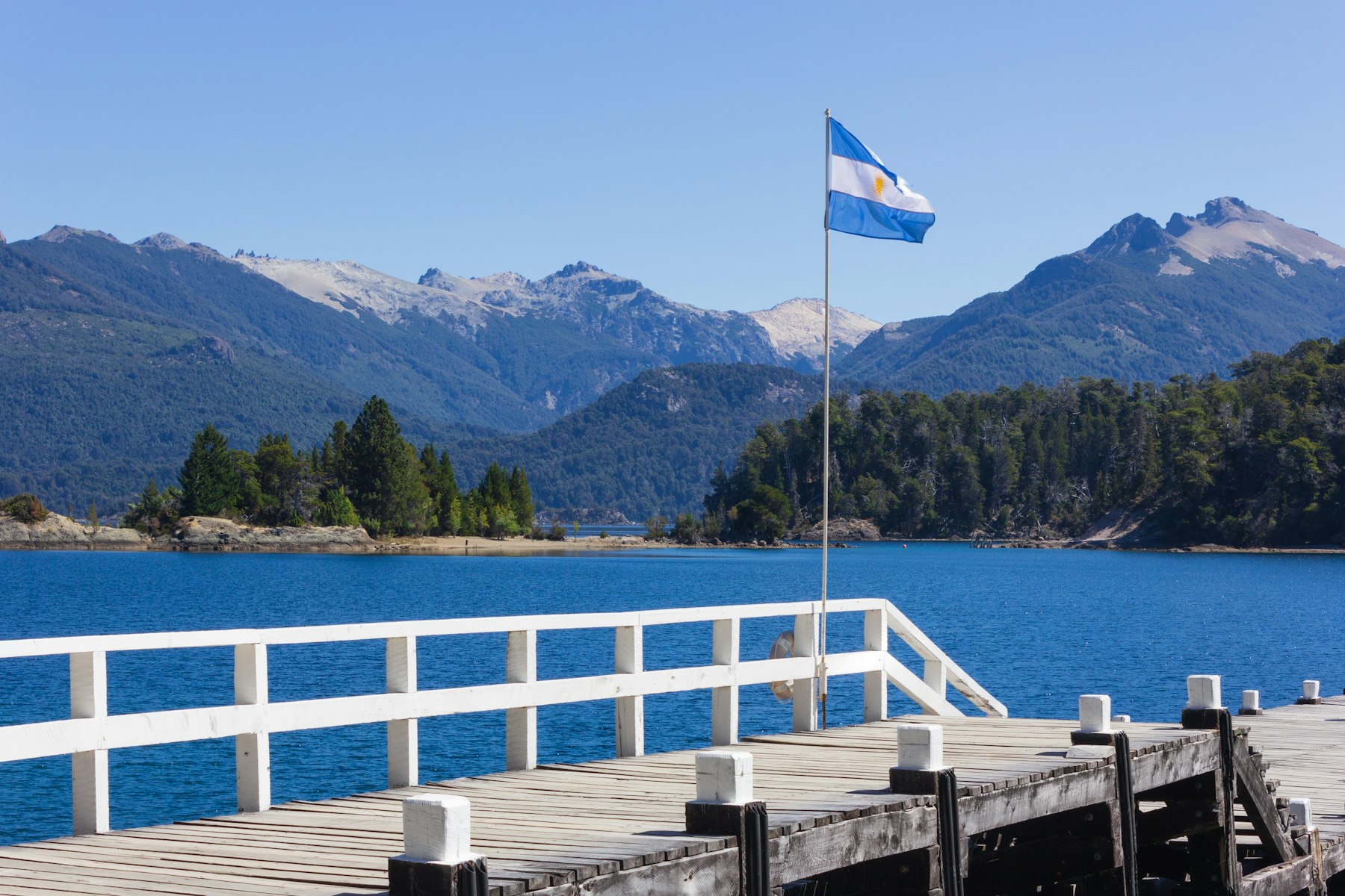 An Argentine flag on a jetty over a lake at Bariloche with mountains behind
