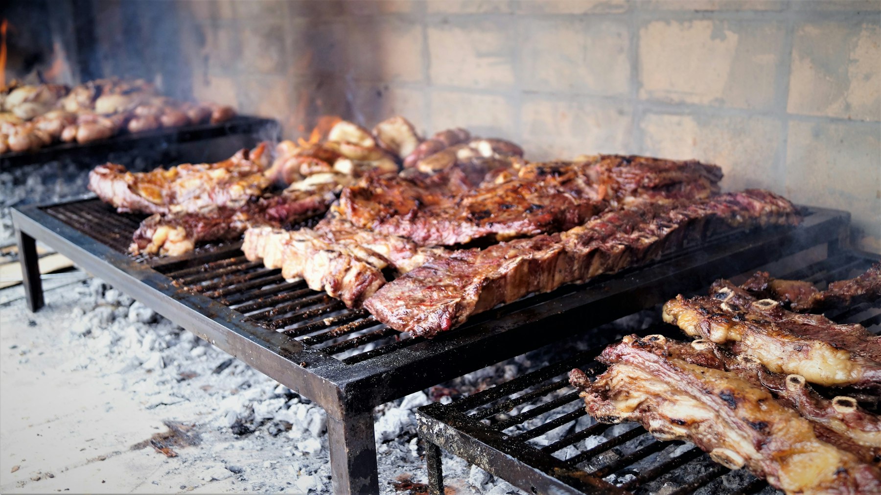 Ribs and cuts of beef cooking slowly over charcoal on an Argentine parrilla
