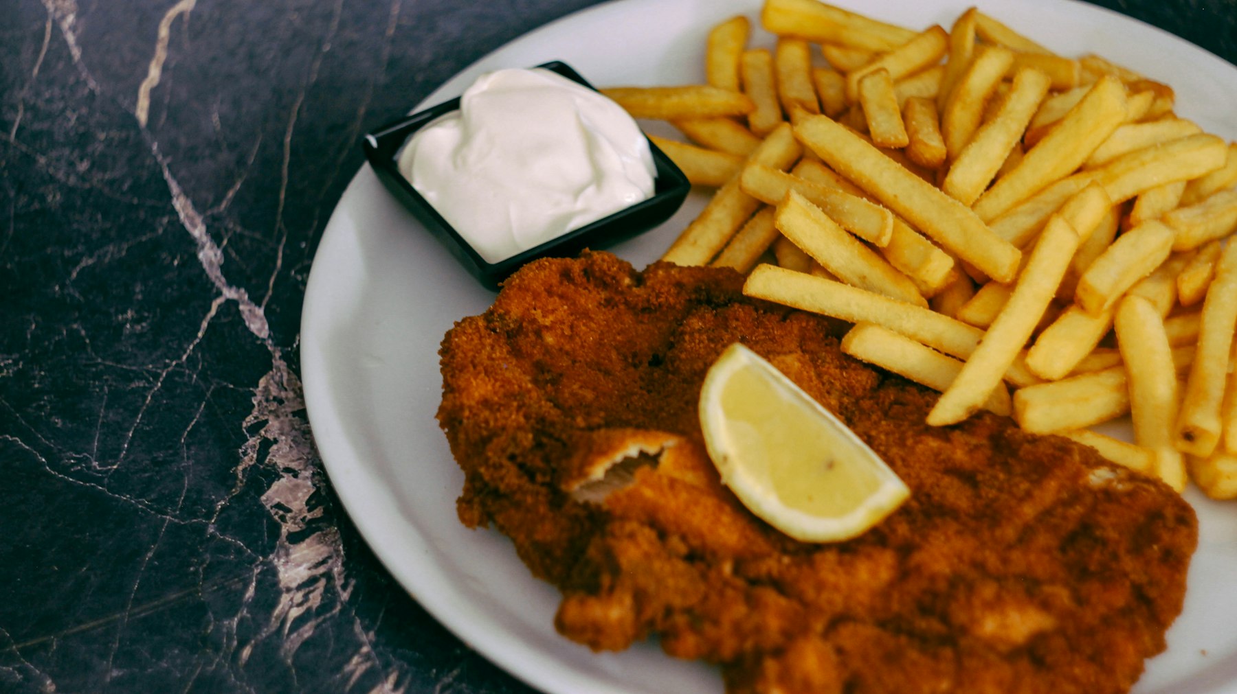 A breaded veal milanesa served with french fries and a lemon wedge