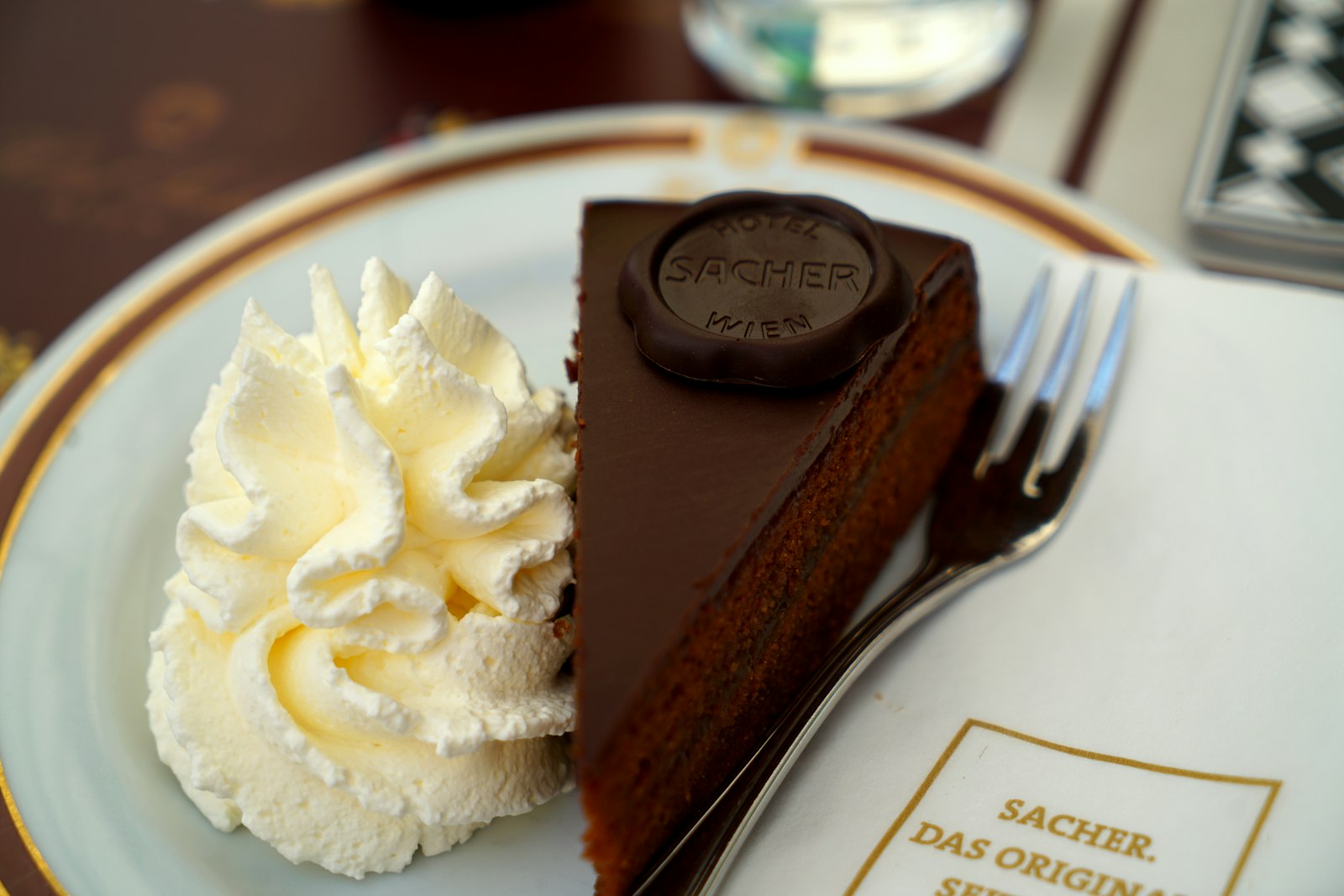 A slice of Sachertorte with apricot jam and dark chocolate glaze beside whipped cream