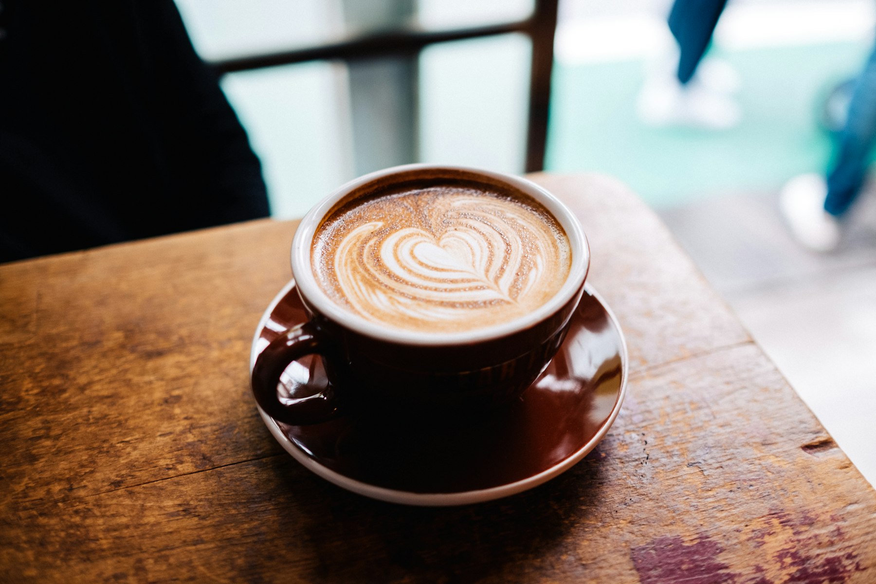 A flat white coffee with latte art in a brown cup