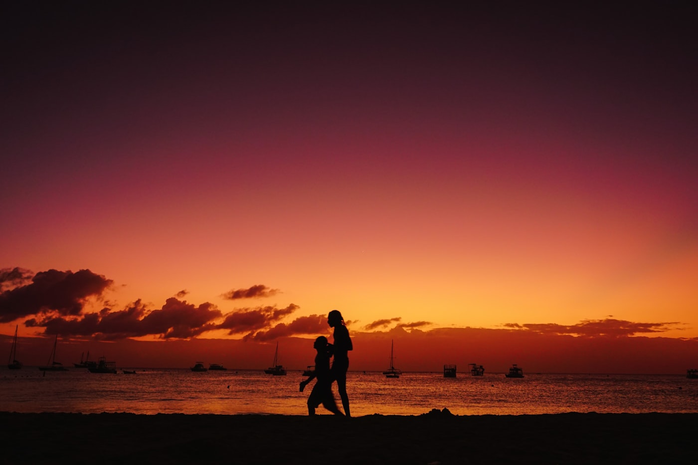 Two people walking along the sand at Carlisle Bay in Bridgetown, Barbados, at sunset