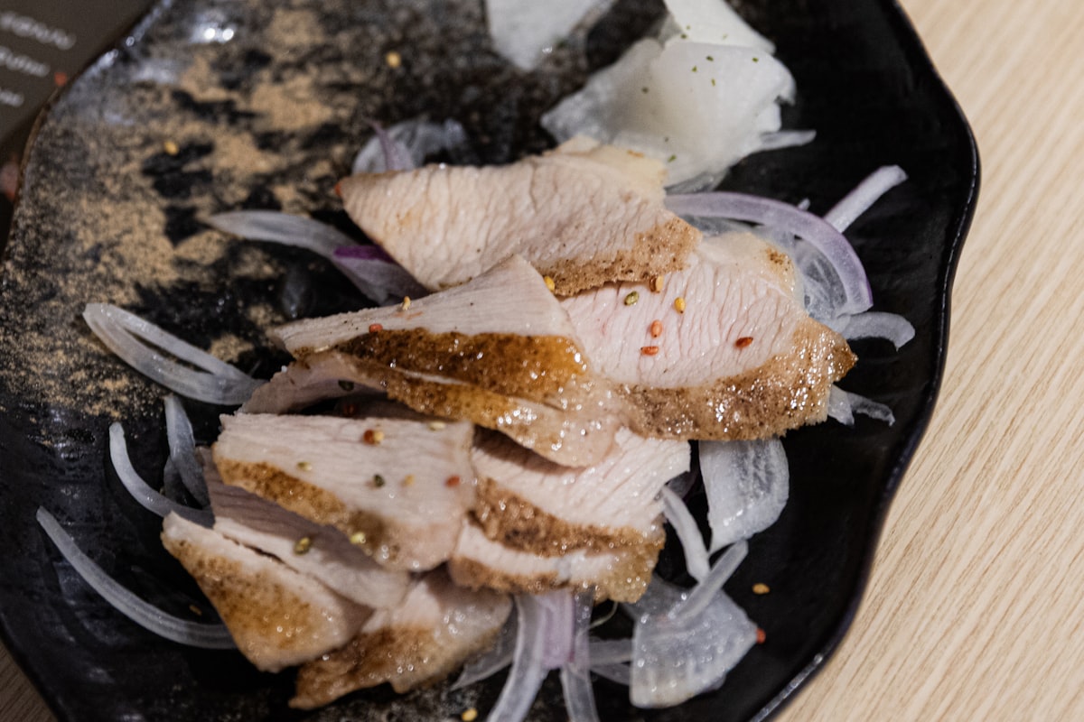 Sliced cooked pork dressed with raw onion and lime on a dark plate