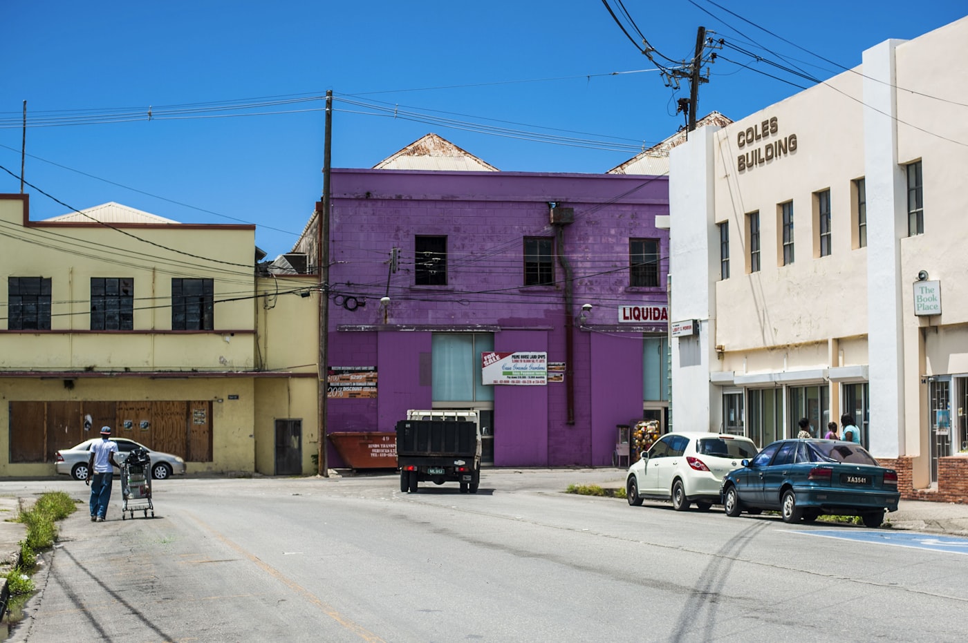 A narrow street lined with parked cars and low buildings in Christ Church on the south coast of Barbados