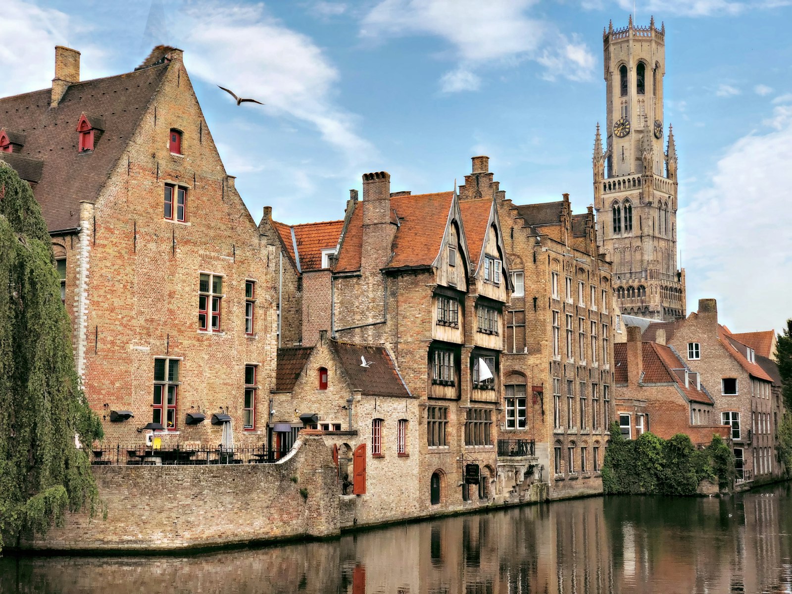 Brick gabled houses and the Belfry tower reflected in a canal at Rozenhoedkaai in Bruges