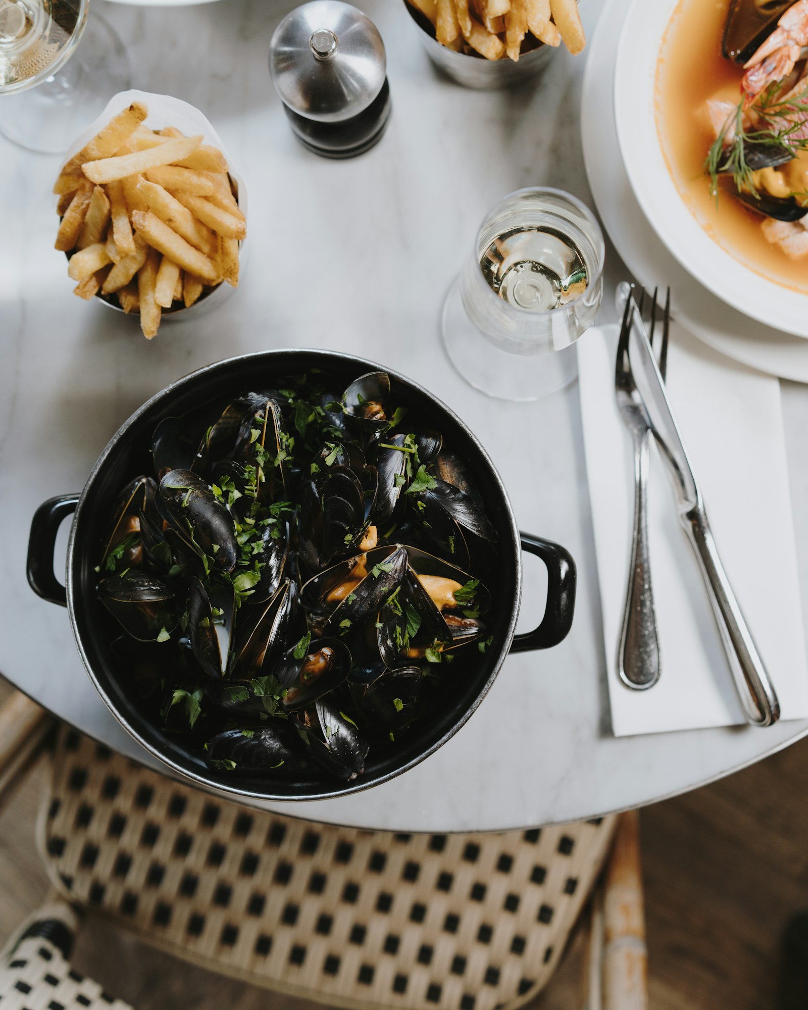 A black pot of steamed mussels with a side of fries on a white tablecloth