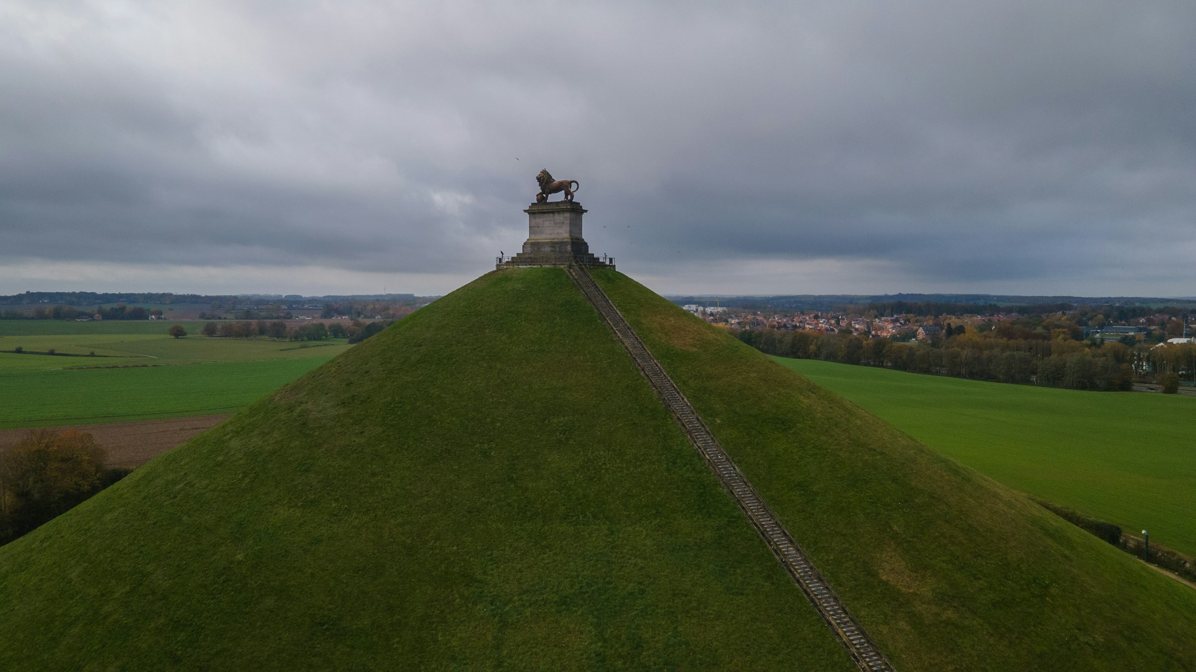 The grass Lion Mound at Waterloo with its long staircase and the lion statue on top above the flat battlefield