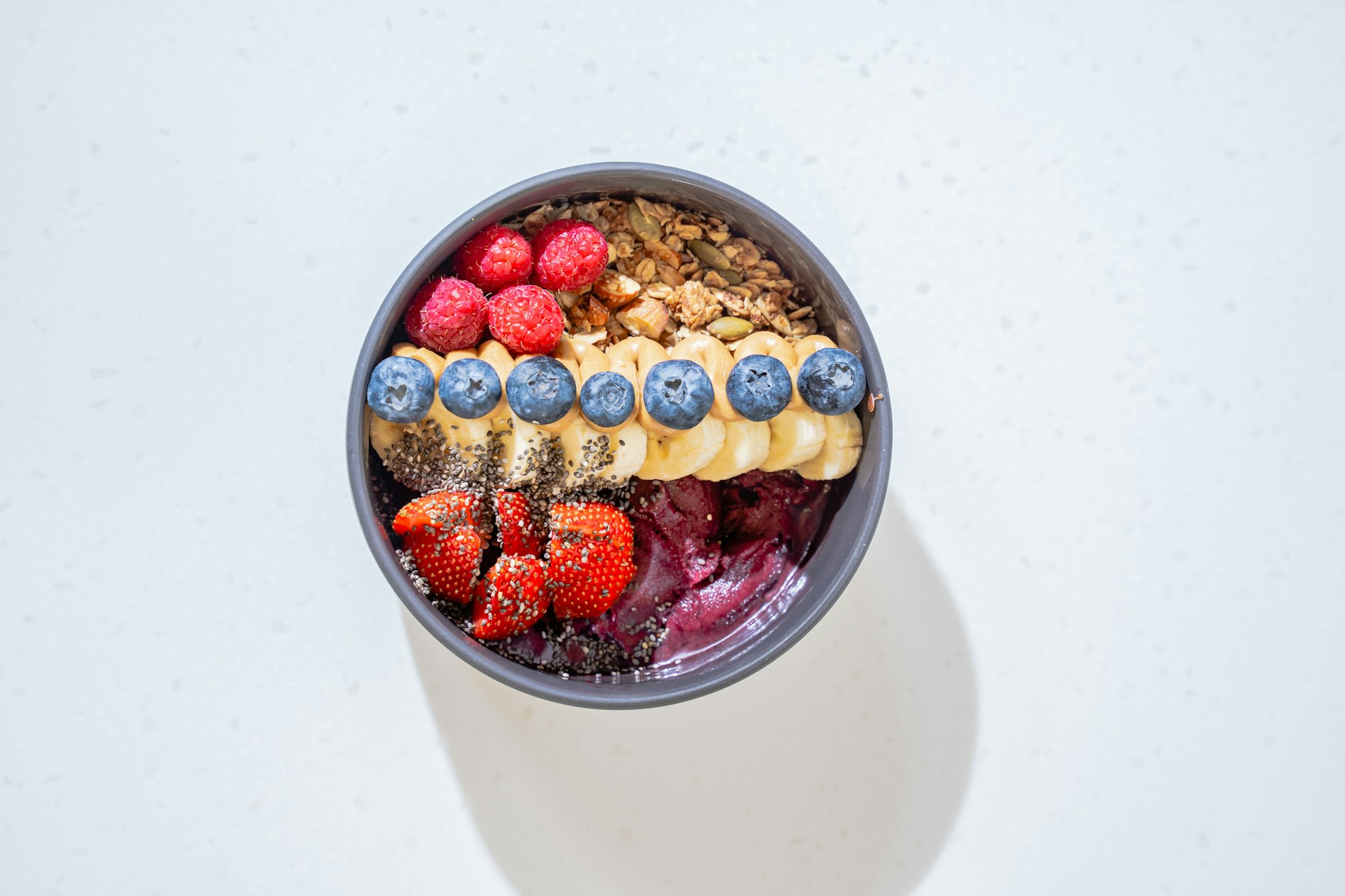A bowl of acai topped with banana strawberries blueberries and granola
