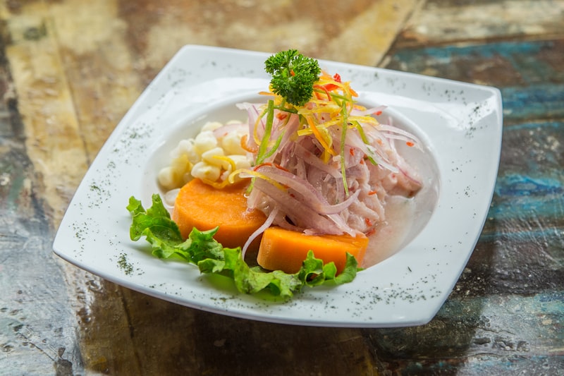 A plate of white fish ceviche with sweet potato, corn and lettuce