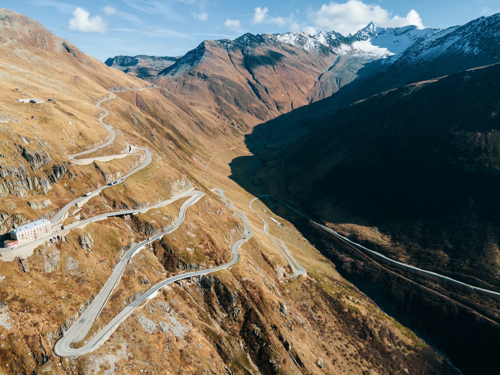 A hairpin mountain pass road switchbacking down a bare Swiss alpine valley