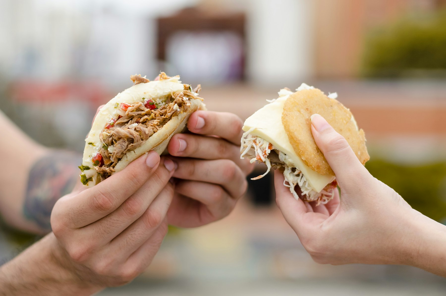 Two hands holding filled Colombian arepas made of corn