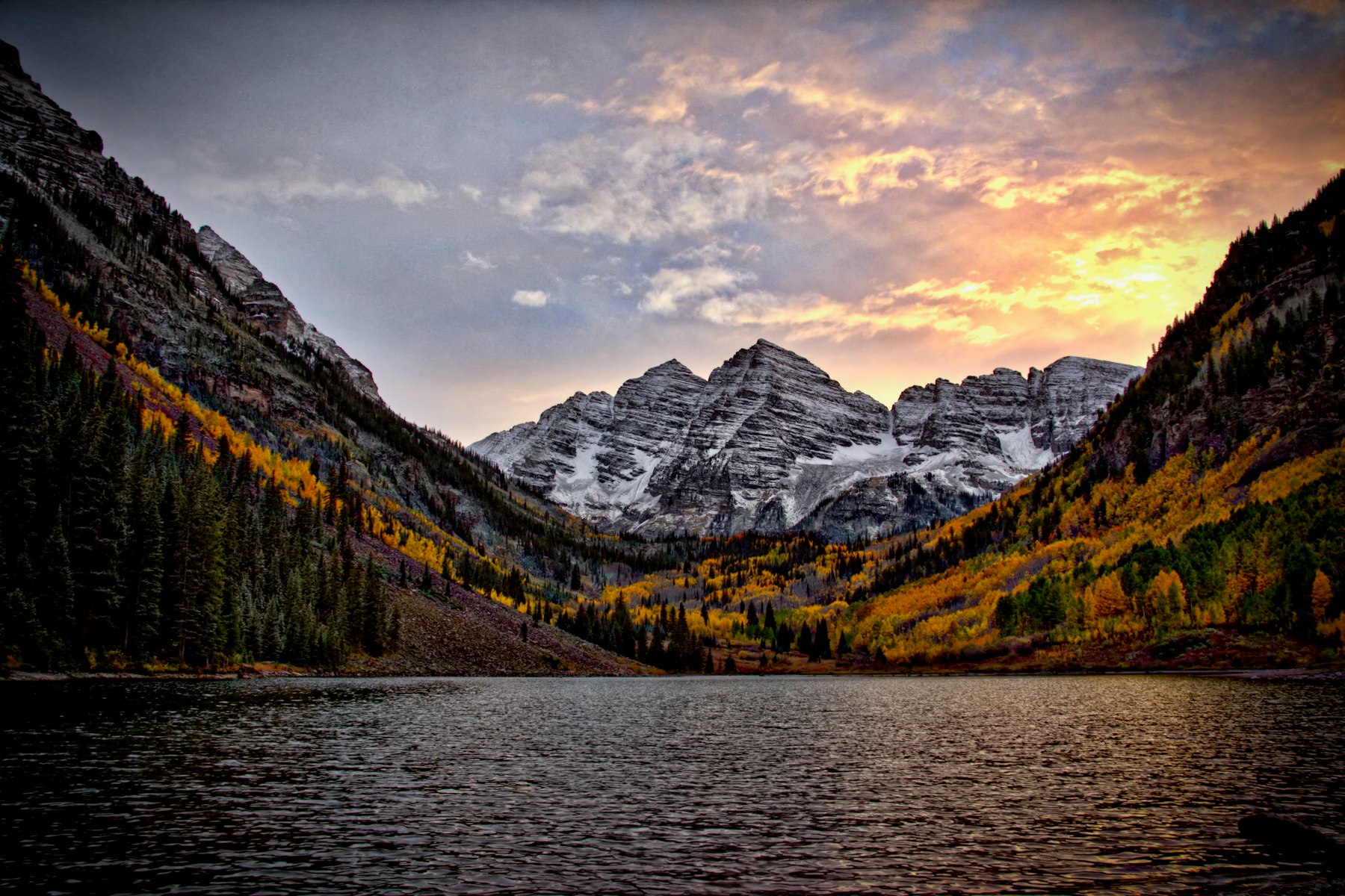 The Maroon Bells peaks reflected in Maroon Lake at sunrise with autumn colour on the slopes