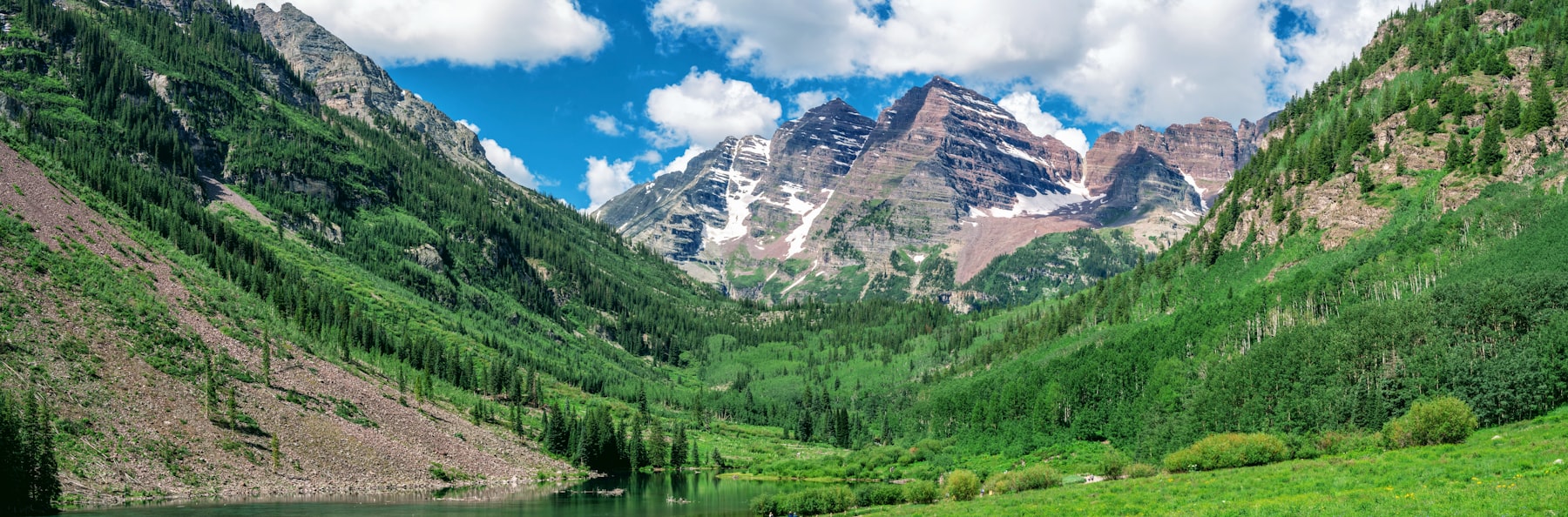 The Maroon Bells rising above a green valley under a blue sky near Aspen Colorado