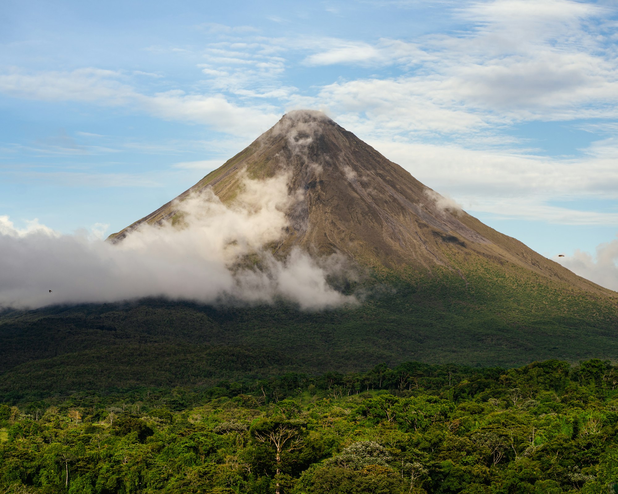 Arenal volcano with a band of cloud around the cone above the rainforest