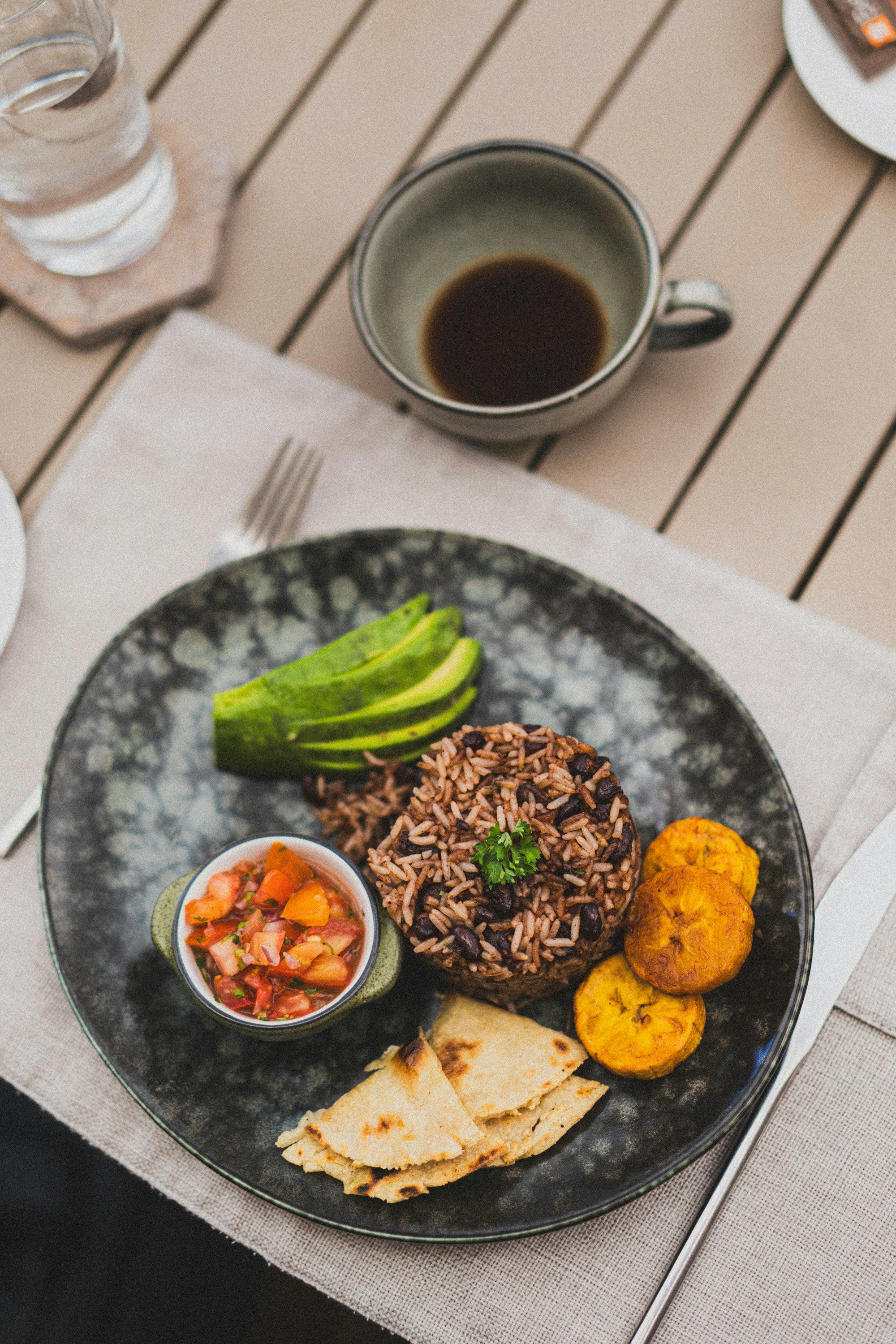 A plate of gallo pinto rice and black beans with sliced avocado and fried plantain