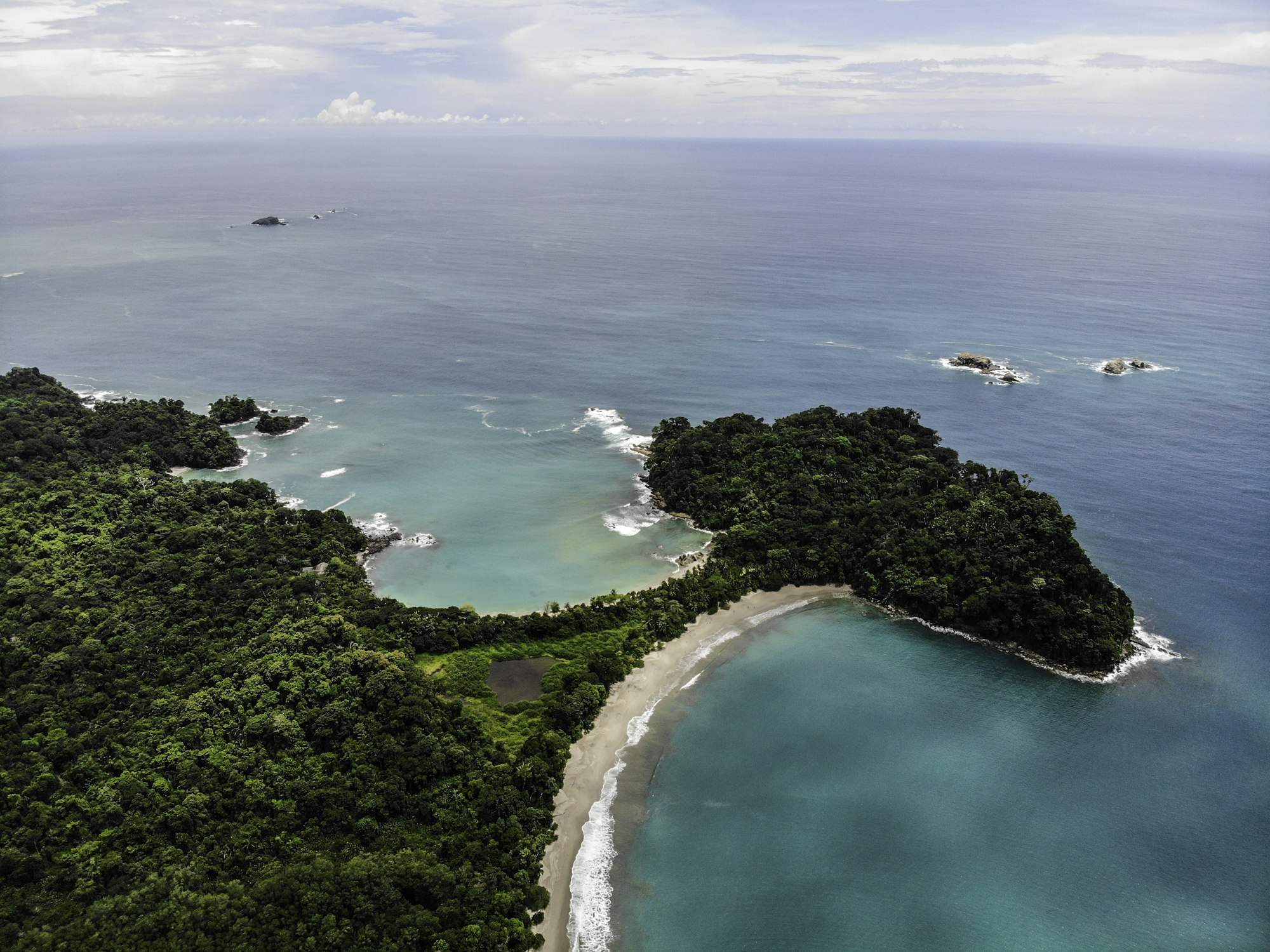 Aerial view of the curved white sand cove and forested headland at Manuel Antonio