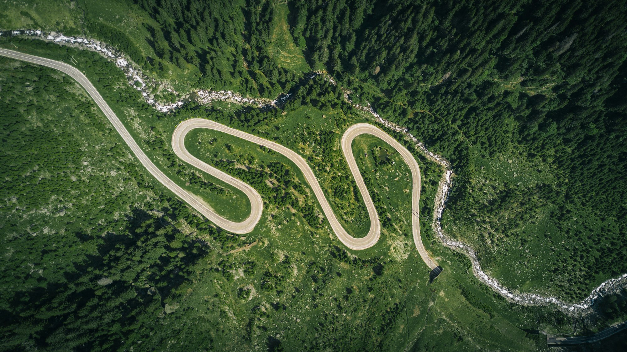 A road switchbacking in tight hairpins down a steep green mountainside seen from above