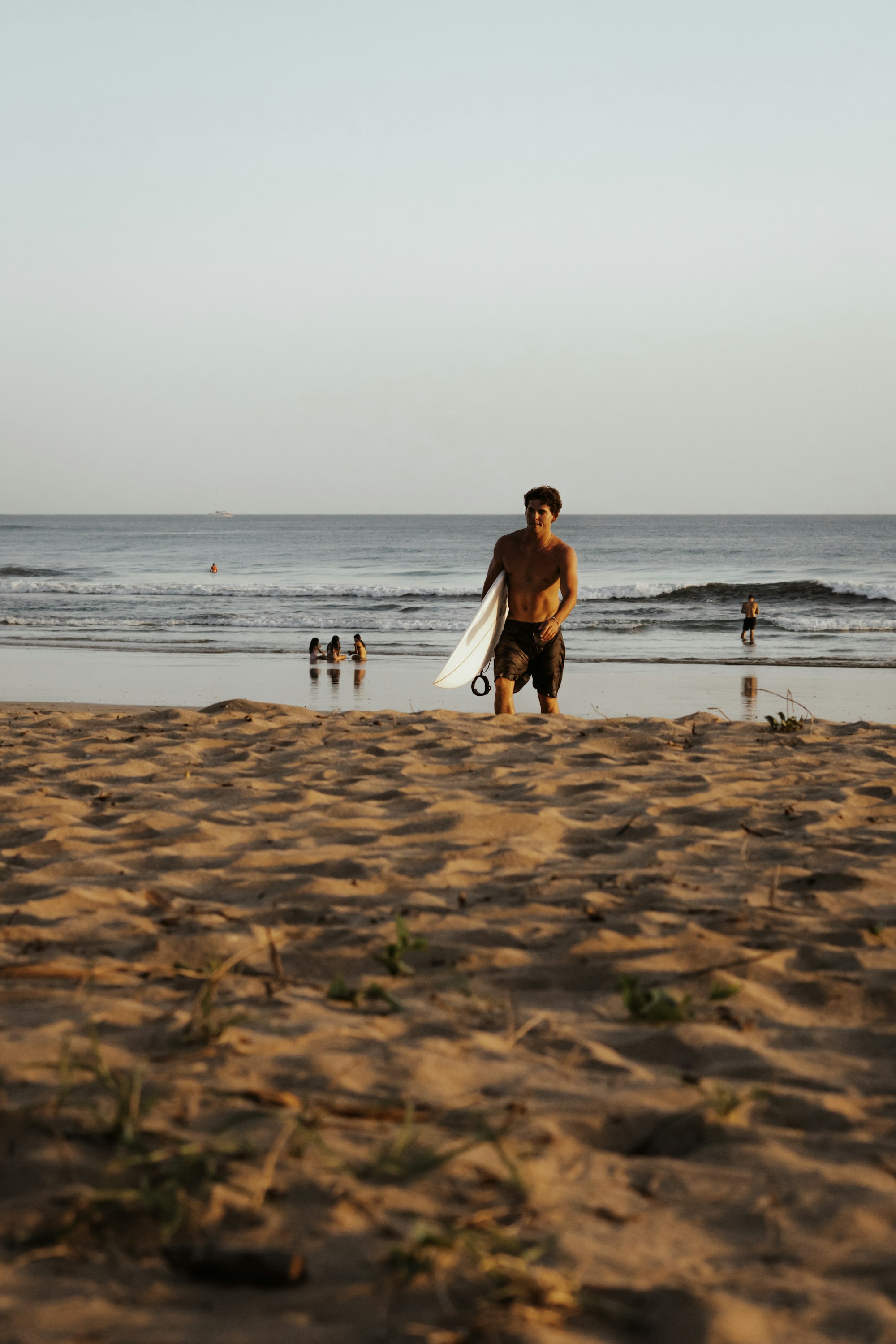 A surfer walking up the sand at Tamarindo with a board under one arm