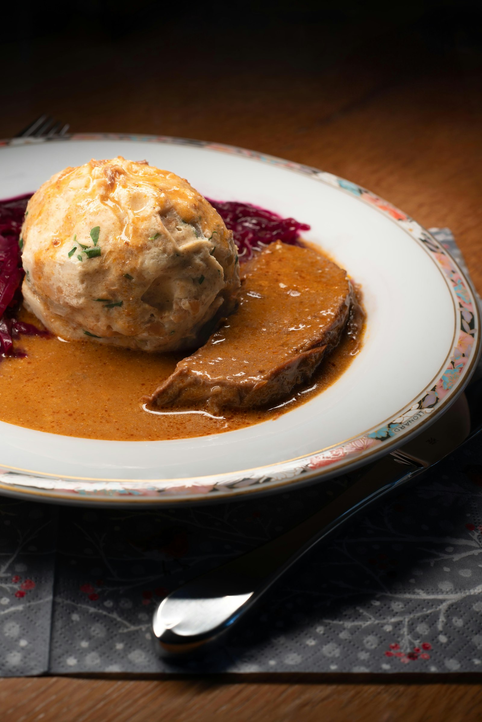 Sliced beef in a pale cream sauce with a bread dumpling and red cabbage on a plate