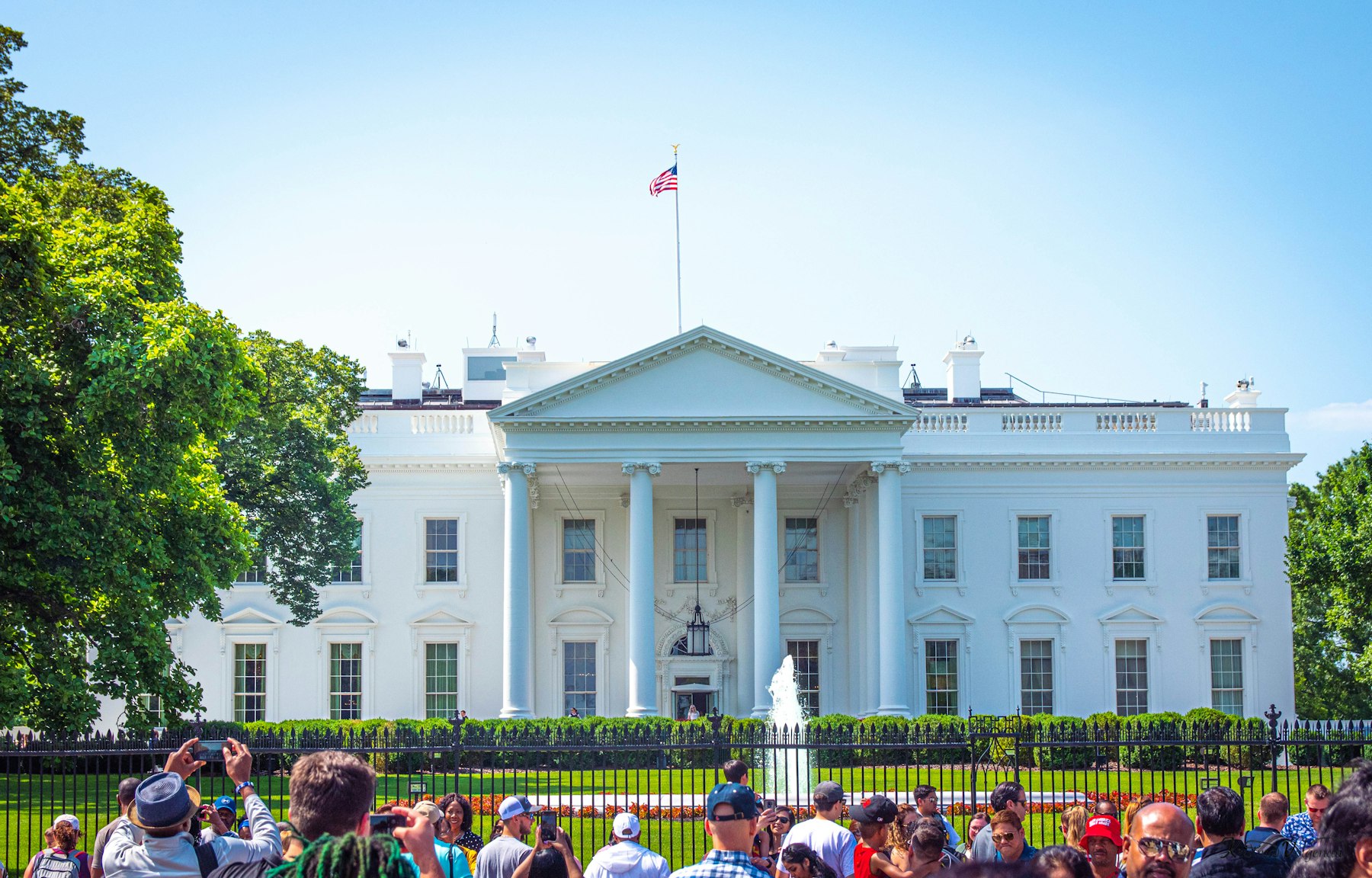 Visitors photographing the White House through the fence on a bright day