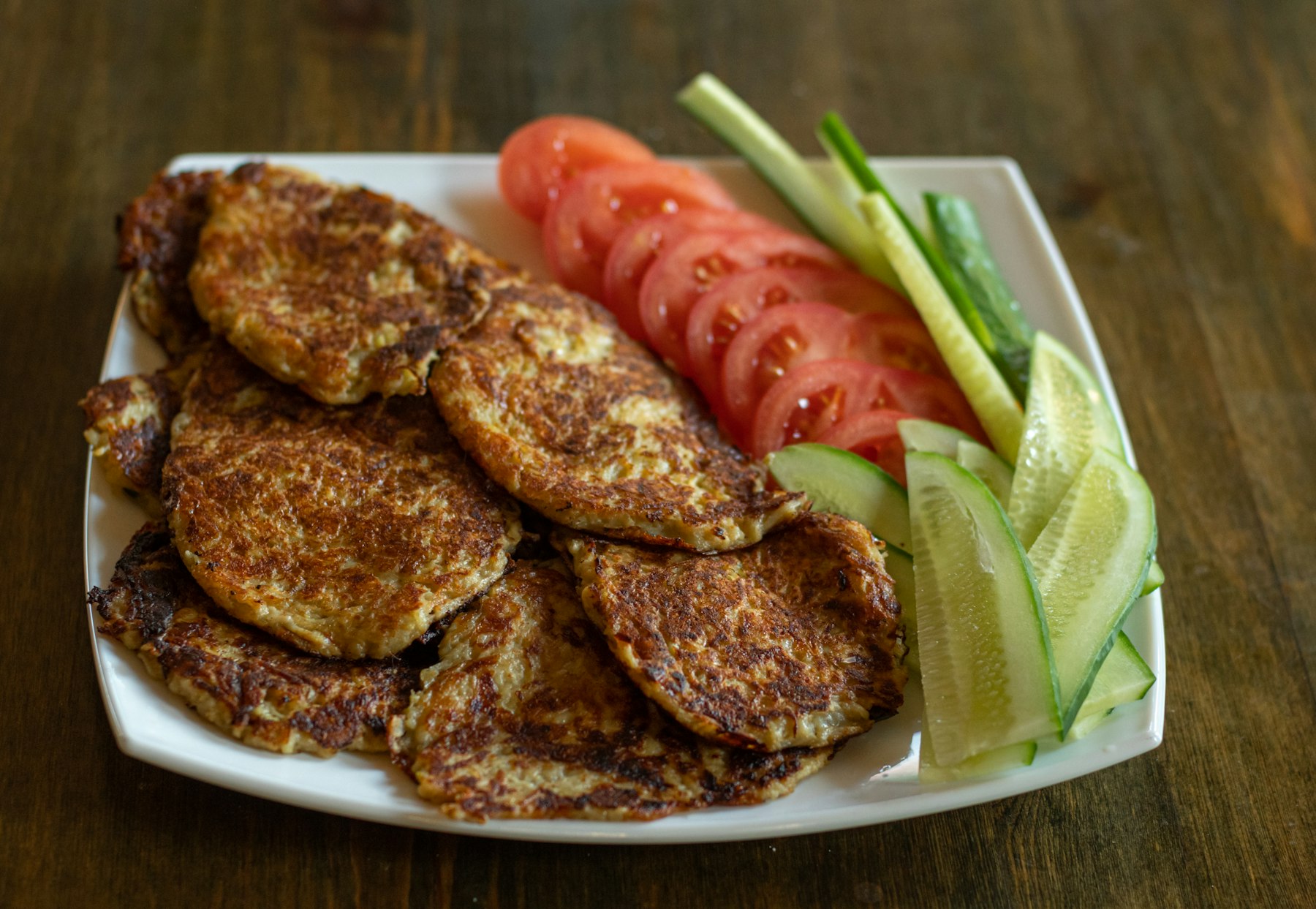 A plate of fried potato patties served with tomato and avocado