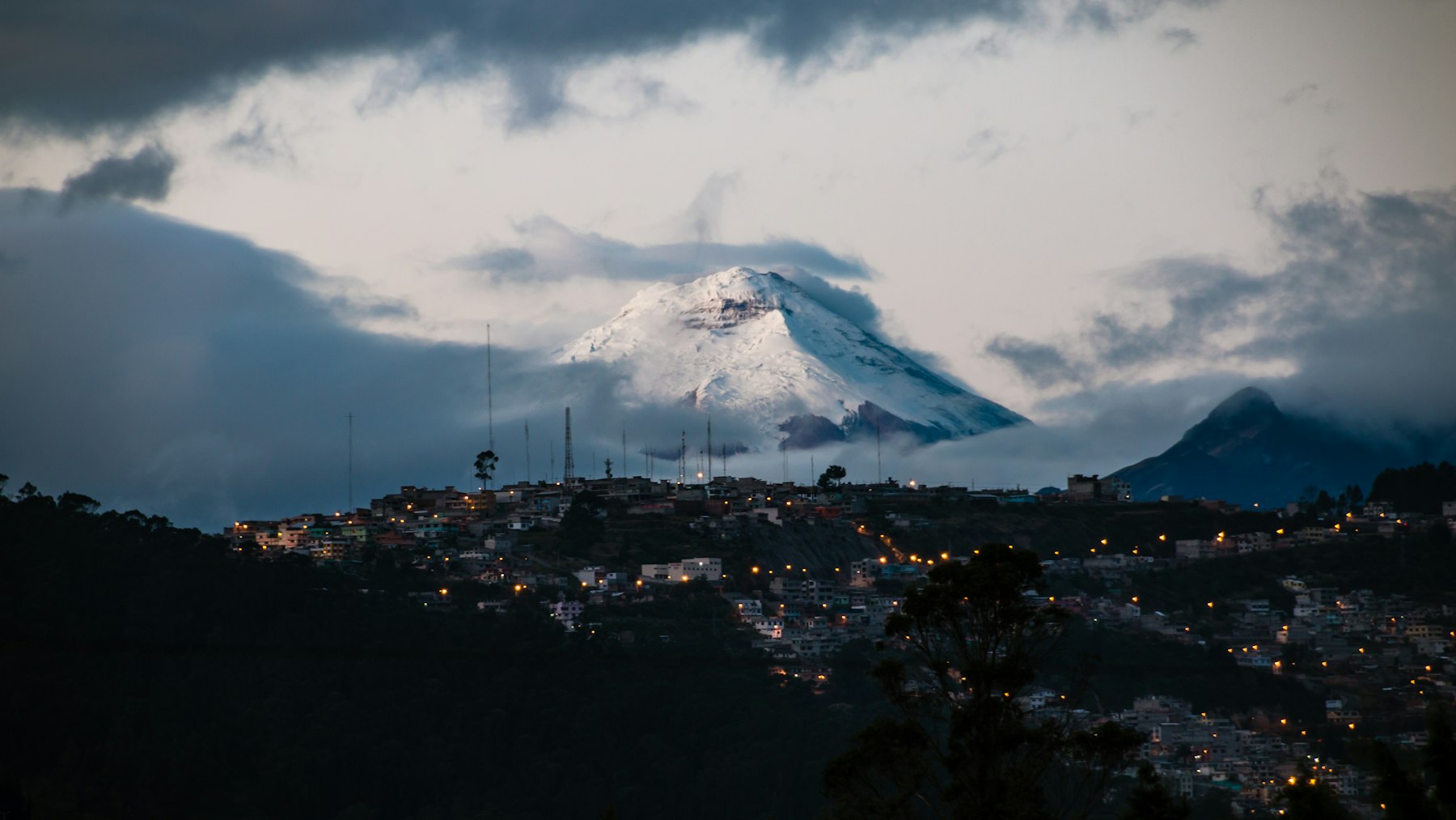 The lights of Quito Ecuador at dusk with a snow capped volcano behind the city