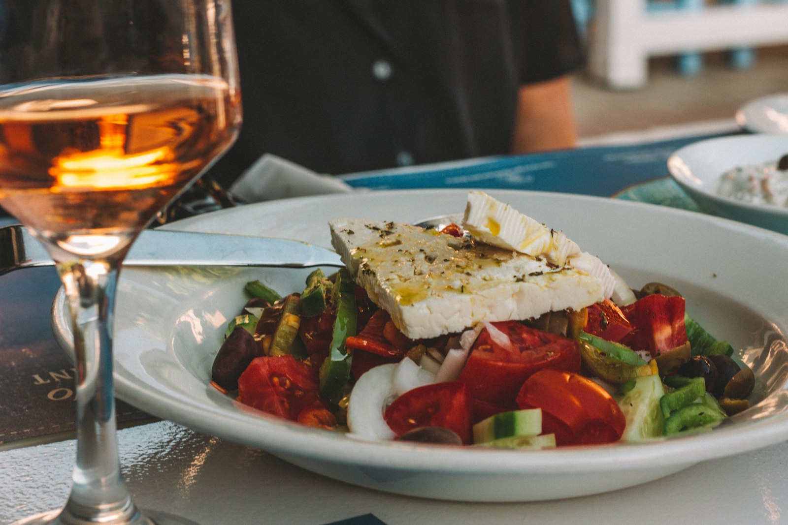 A Greek salad of tomato, cucumber, olives and a slab of feta on a white plate