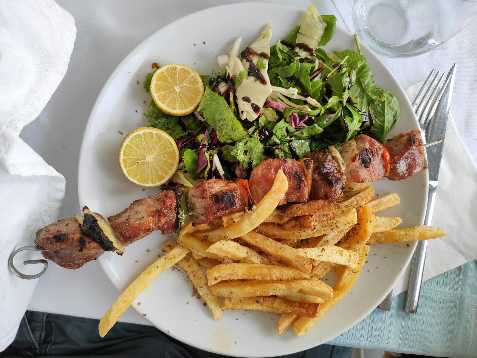 A plate of grilled souvlaki skewers with fries, salad and lemon