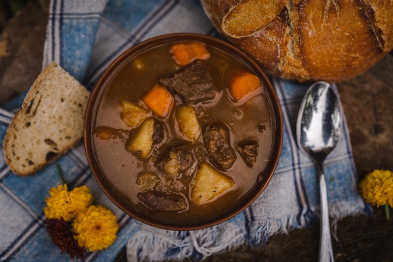 A bowl of dark meat and potato stew with bread beside it