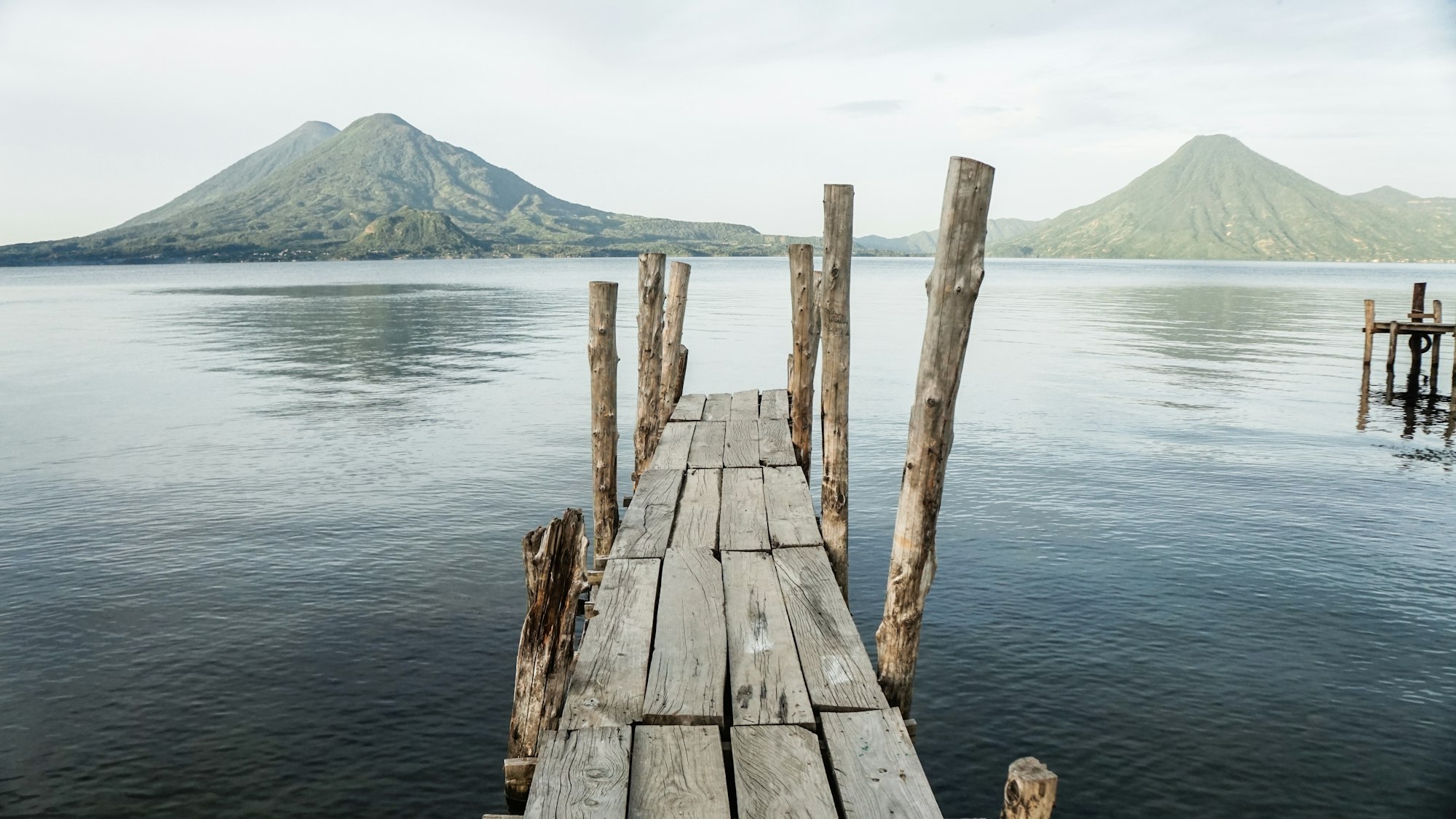 Volcanoes across the water at Lake Atitlan with an old wooden dock in the foreground