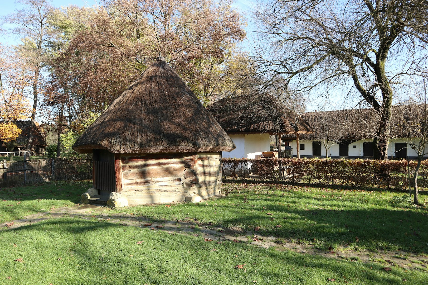 Whitewashed village houses with steep thatched roofs and wooden fences along a dirt lane in a Hungarian village