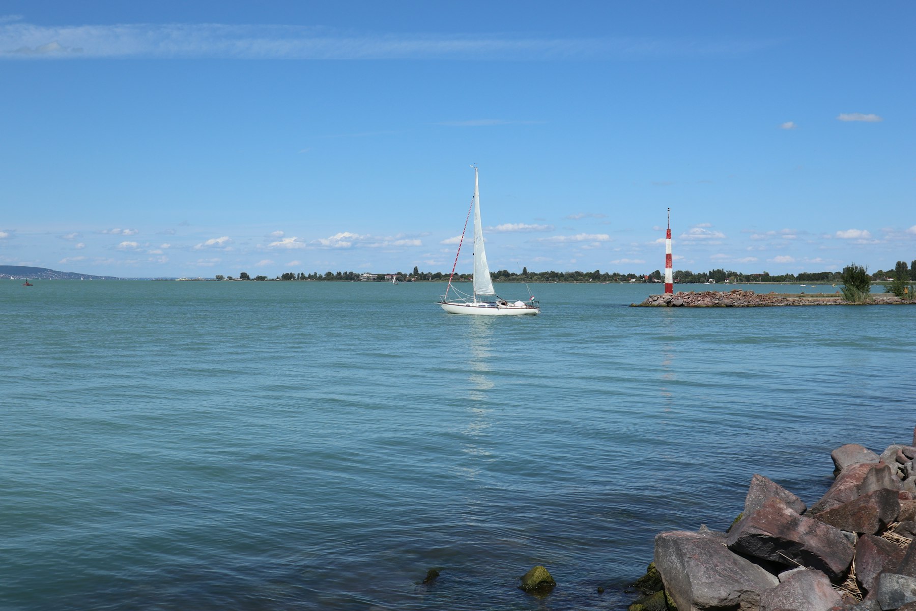 A white sailboat on the flat blue water of Lake Balaton in Hungary on a clear summer day
