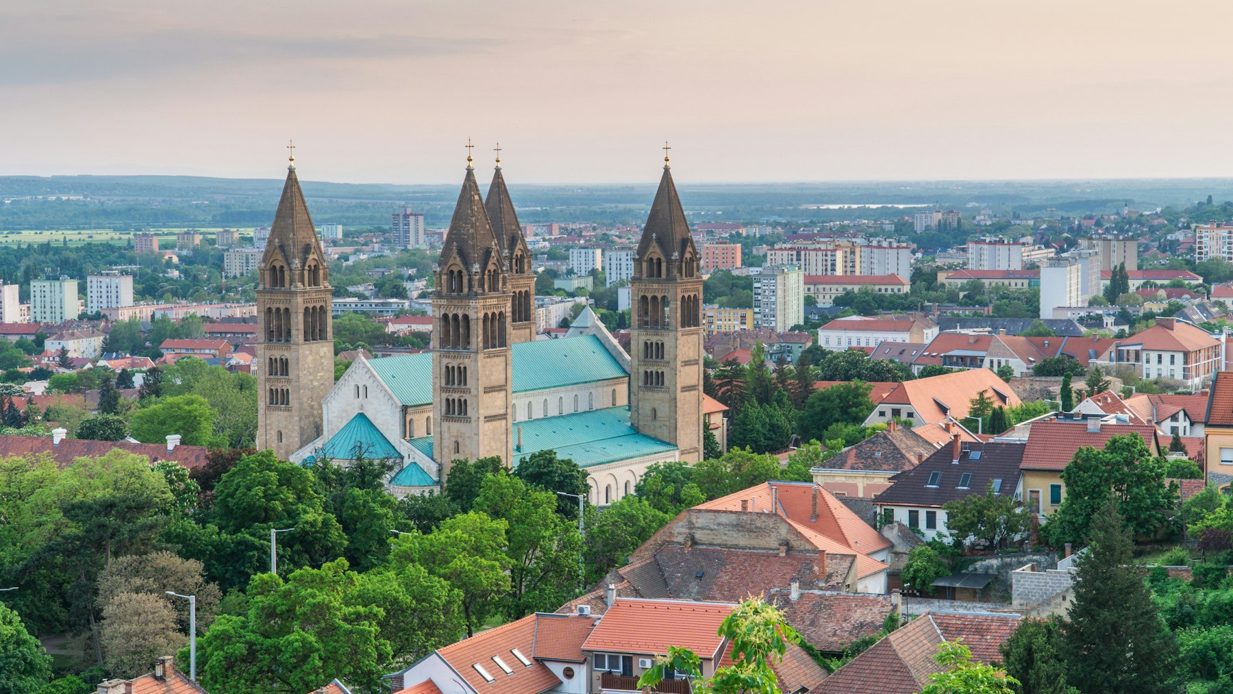 The four towers of Pecs Cathedral rising above the red tiled rooftops of the town with green hills behind