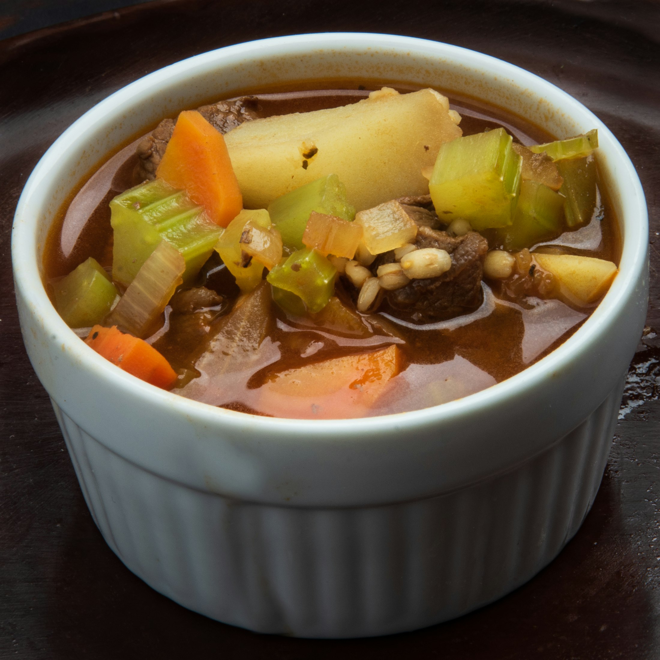 A white bowl of lamb and root vegetable soup with carrot and potato