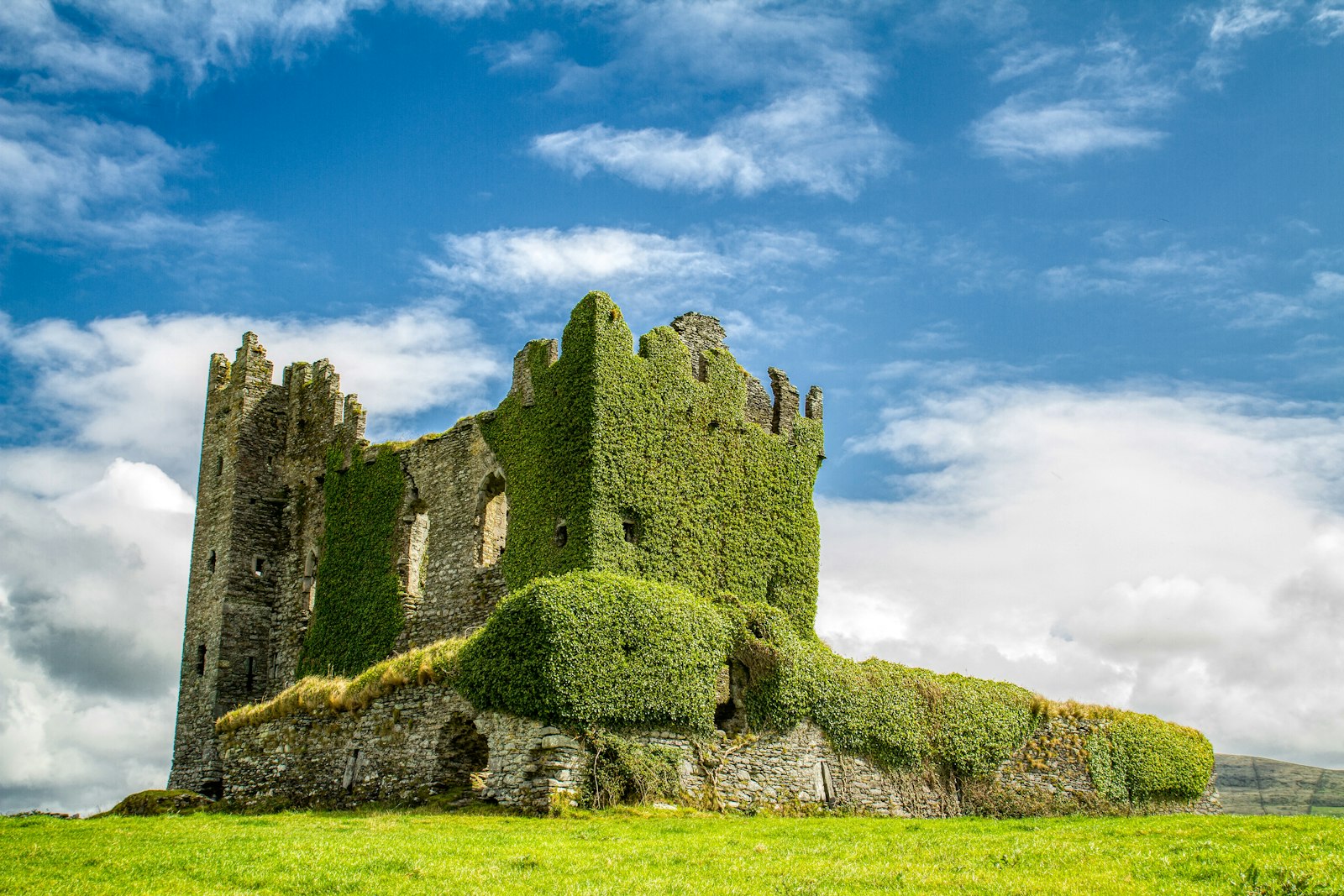 A ruined stone castle overgrown with ivy standing in a green field under a bright sky