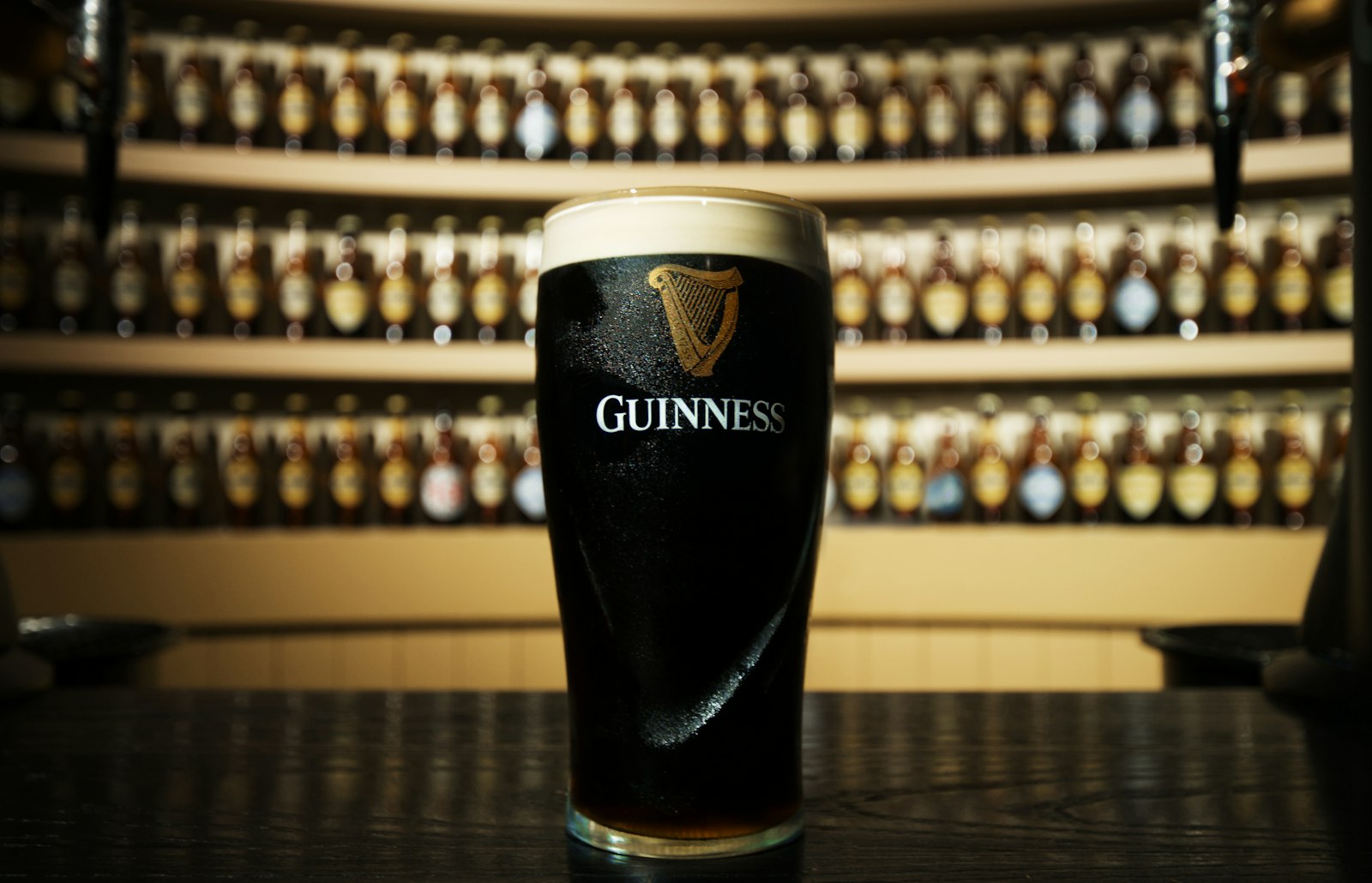 A pint of dark stout with a thick cream head standing on a bar