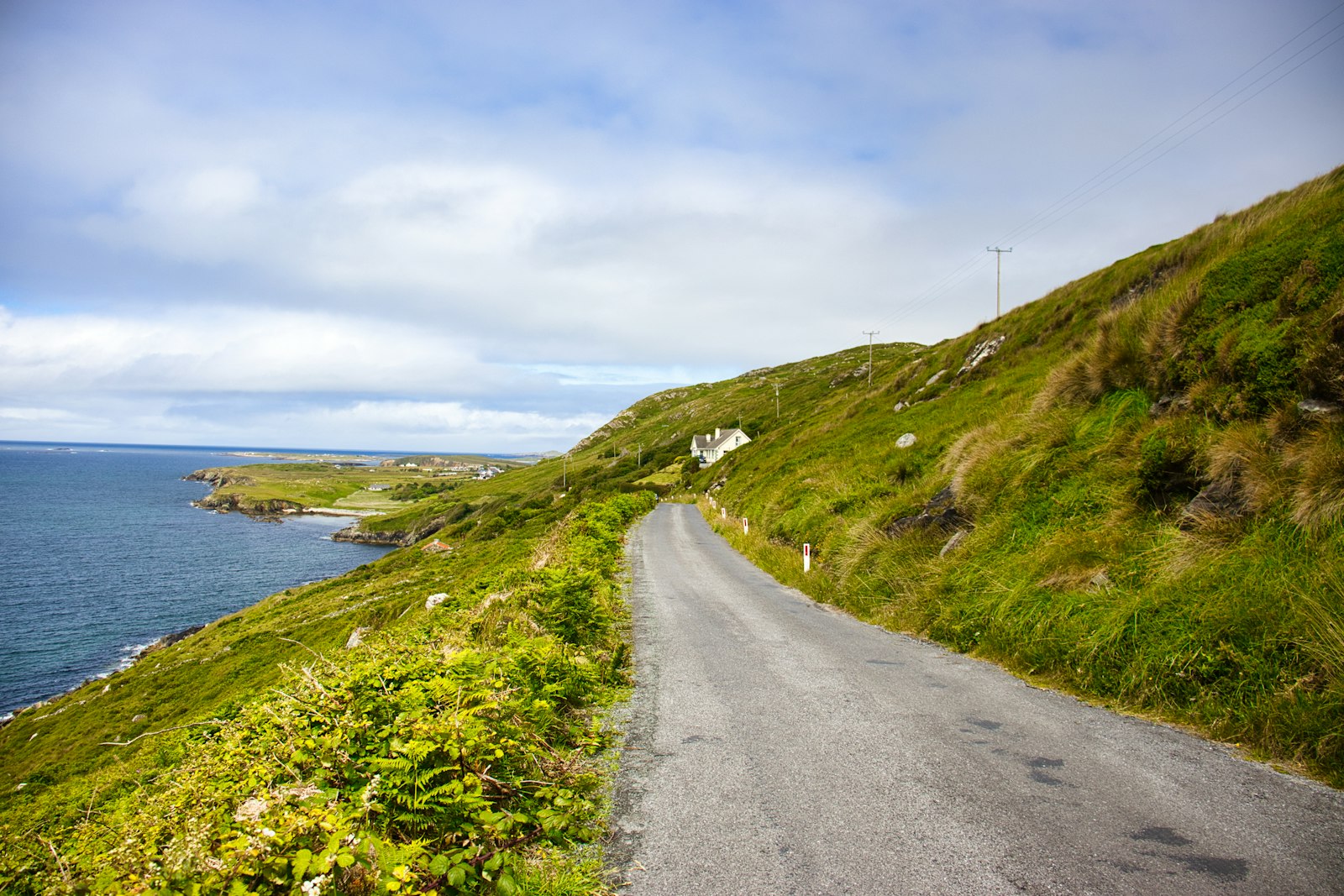 A narrow coastal road running along a green hillside above the Atlantic in Ireland