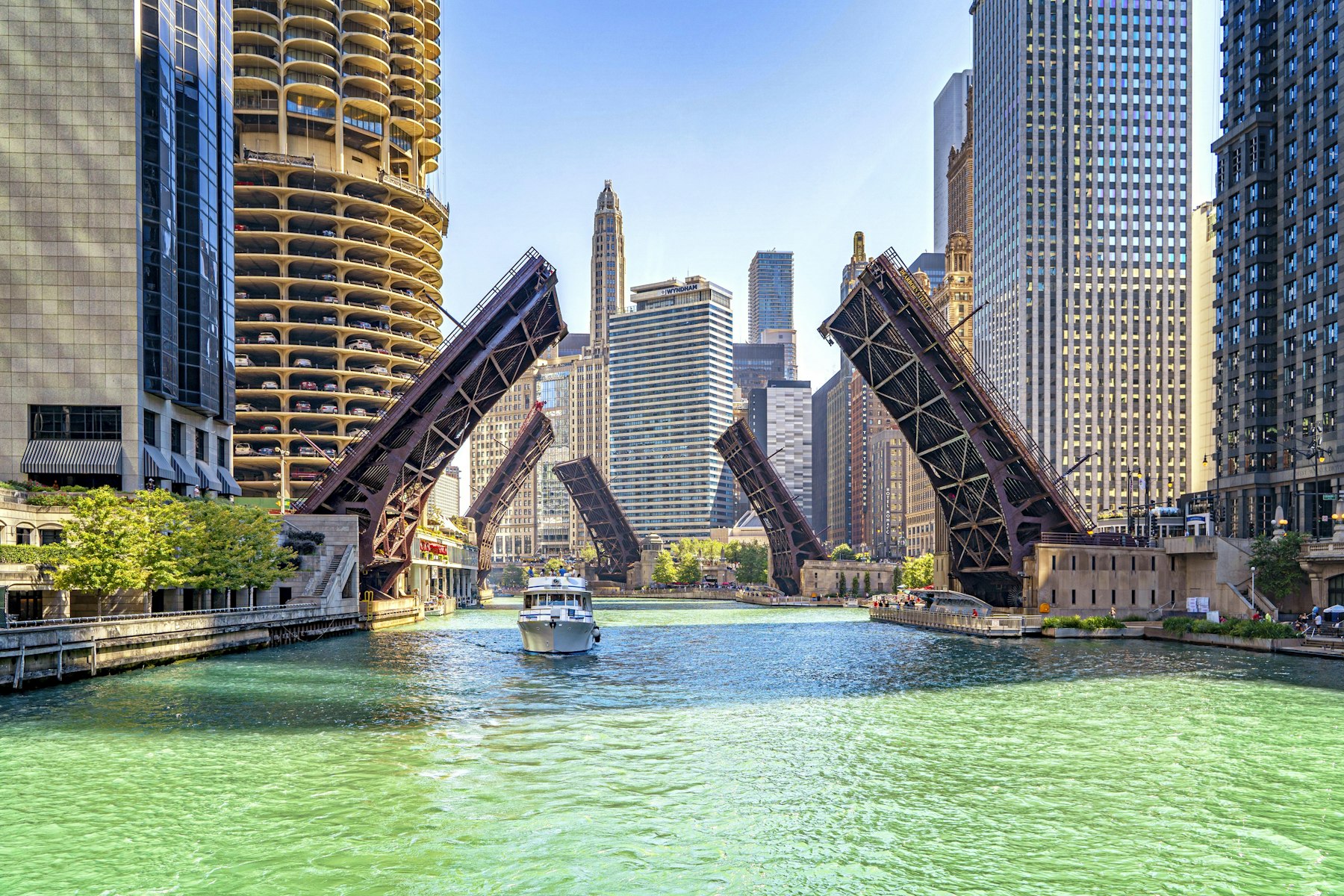 A tour boat on the Chicago River passing beneath raised bascule bridges between skyscrapers
