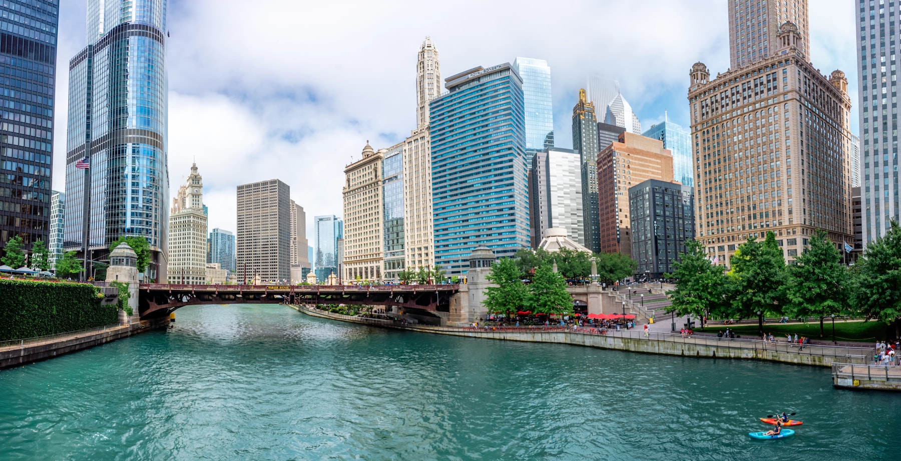 The Chicago River running between skyscrapers with green trees along the riverwalk