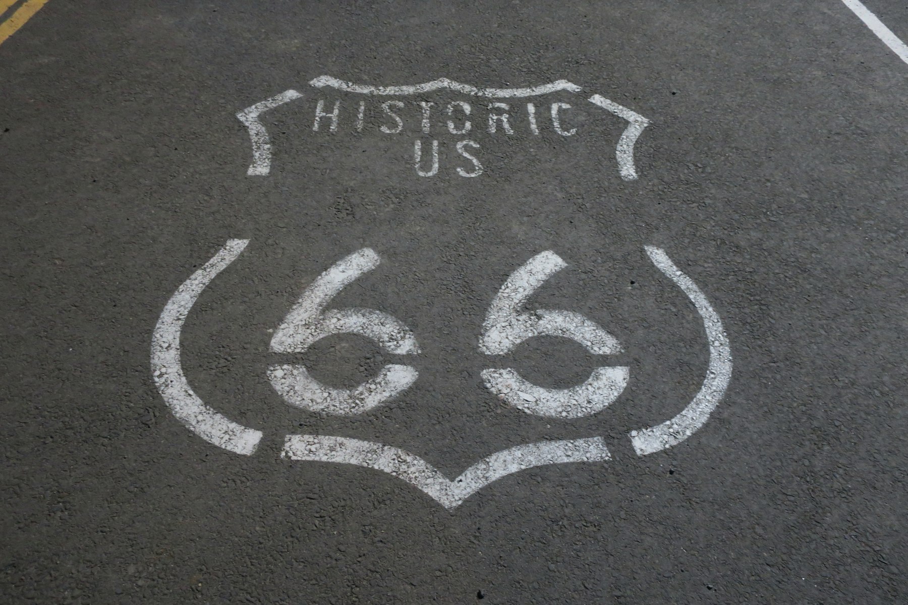 A historic US 66 highway shield painted in white on grey asphalt