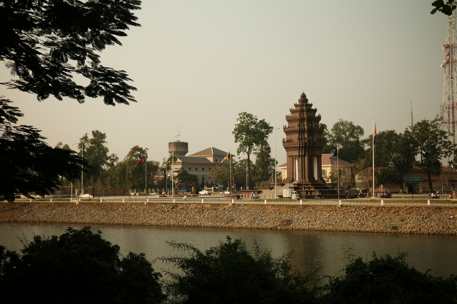 A monument and colonial buildings on the riverbank in a provincial Cambodian town at dusk