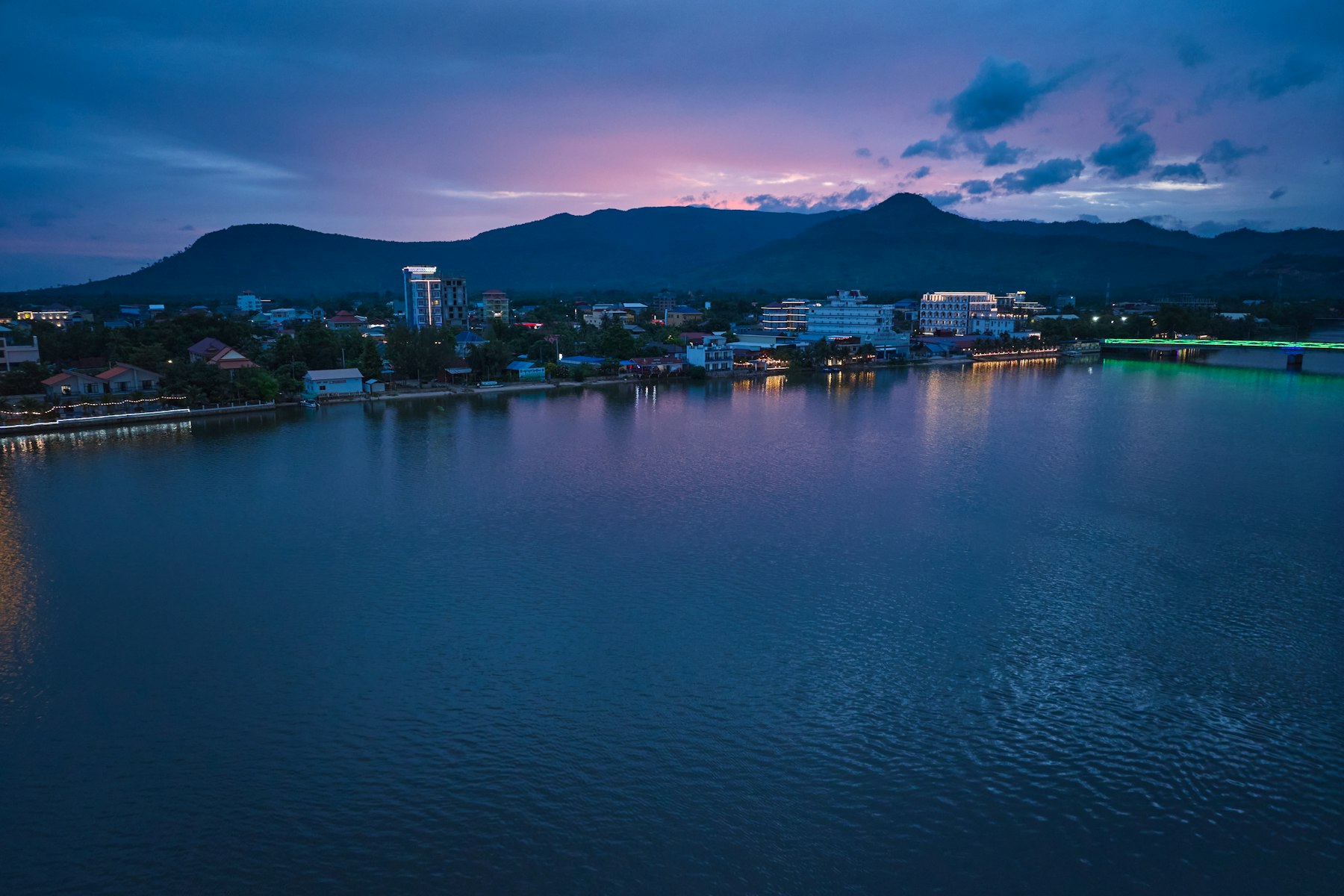 The riverfront at Kampot lit up at dusk with the Bokor hills behind