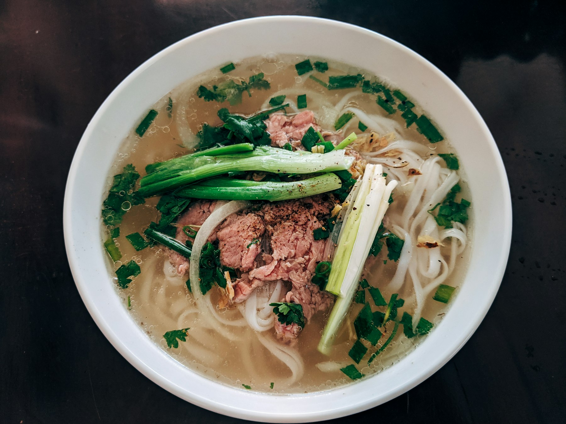 A bowl of kuy teav, Cambodian rice noodle soup with pork, spring onion and fresh greens