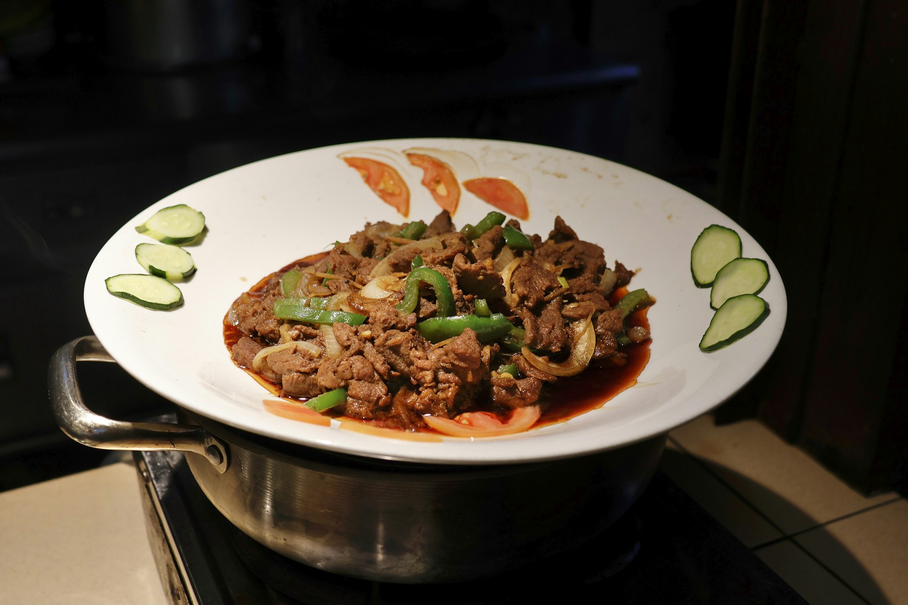 Beef lok lak, cubes of stir fried beef on a plate with sliced cucumber and tomato